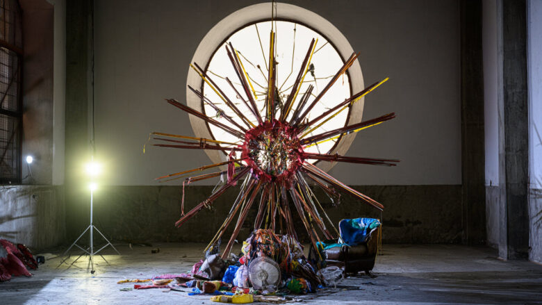 A large sunburst sculpture made of red and yellow wooden slats in a warehouse art installation