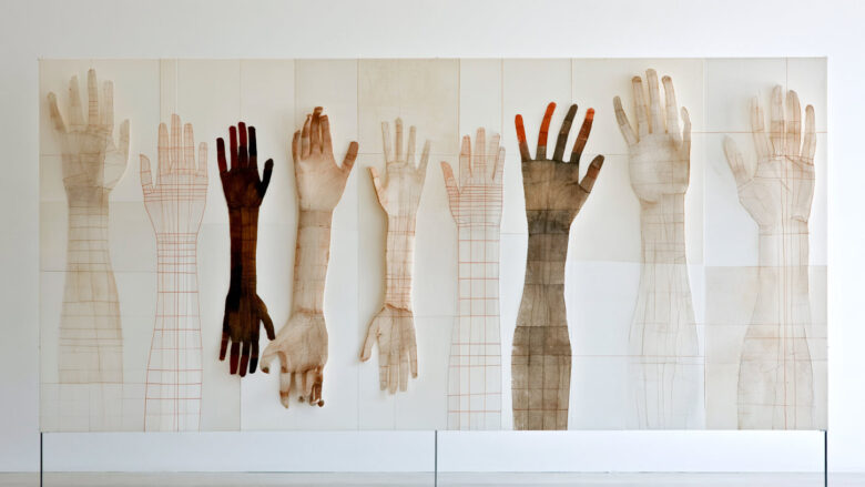 Installation of ten paper hands and arms in different skin tones raised against a white wall
