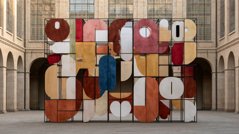 Abstract sculptural installation of colourful rounded shapes in a black metal grid inside a stone courtyard