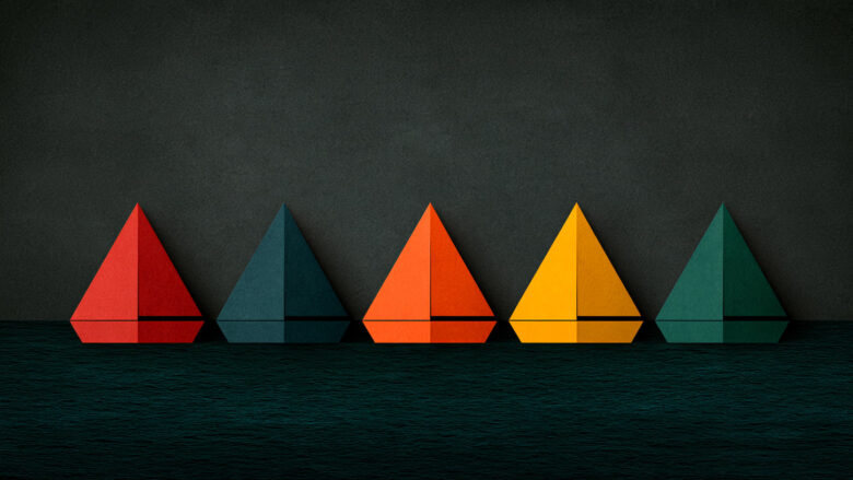 Five folded paper sailboats in red, teal, orange, yellow and green on dark water